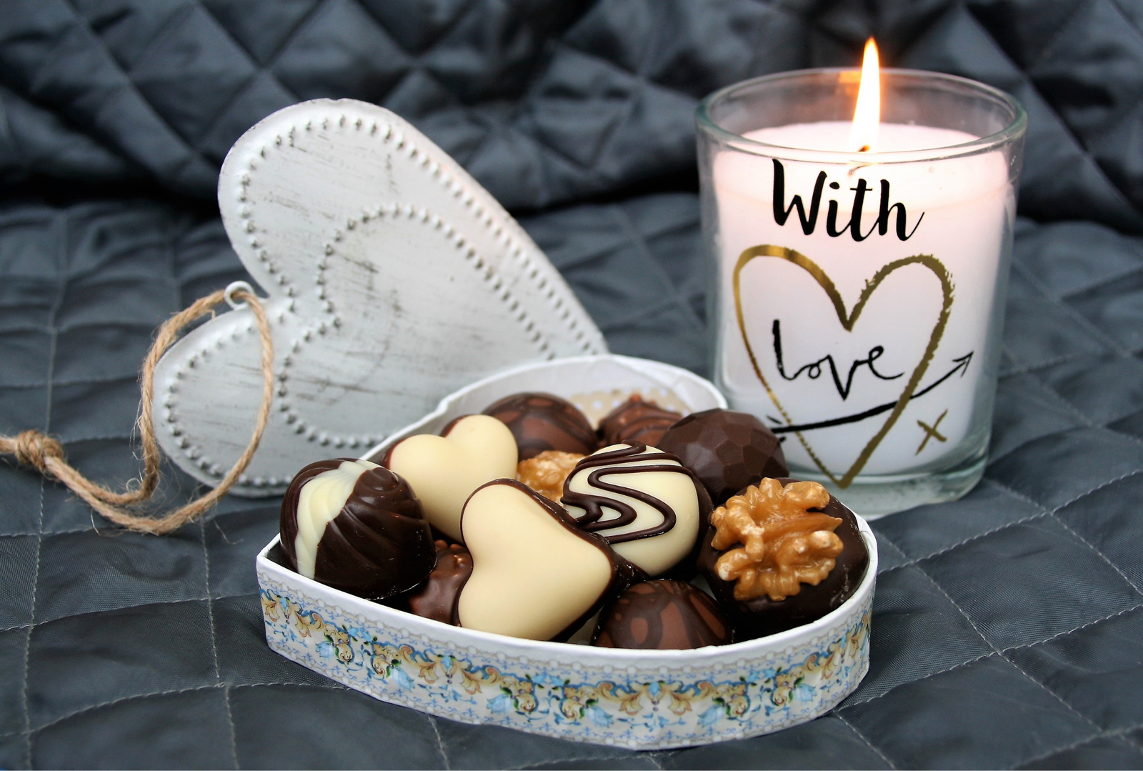 A candle that is labeled with love and chocolates in a box sitting on a bed.