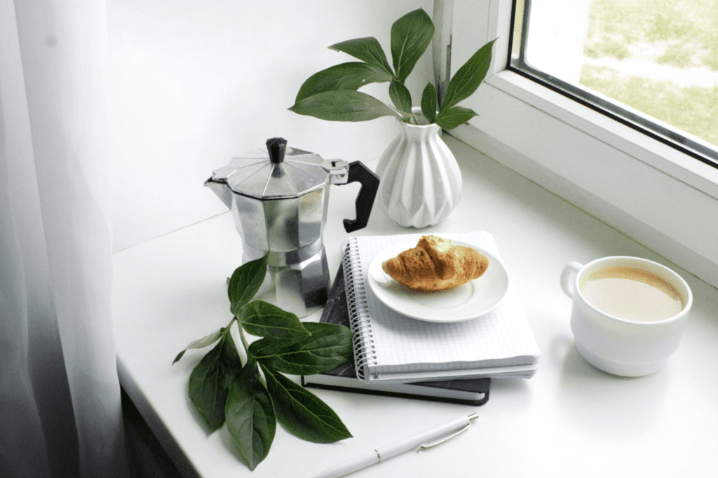 A coffee pitcher, food, and drink by the window.