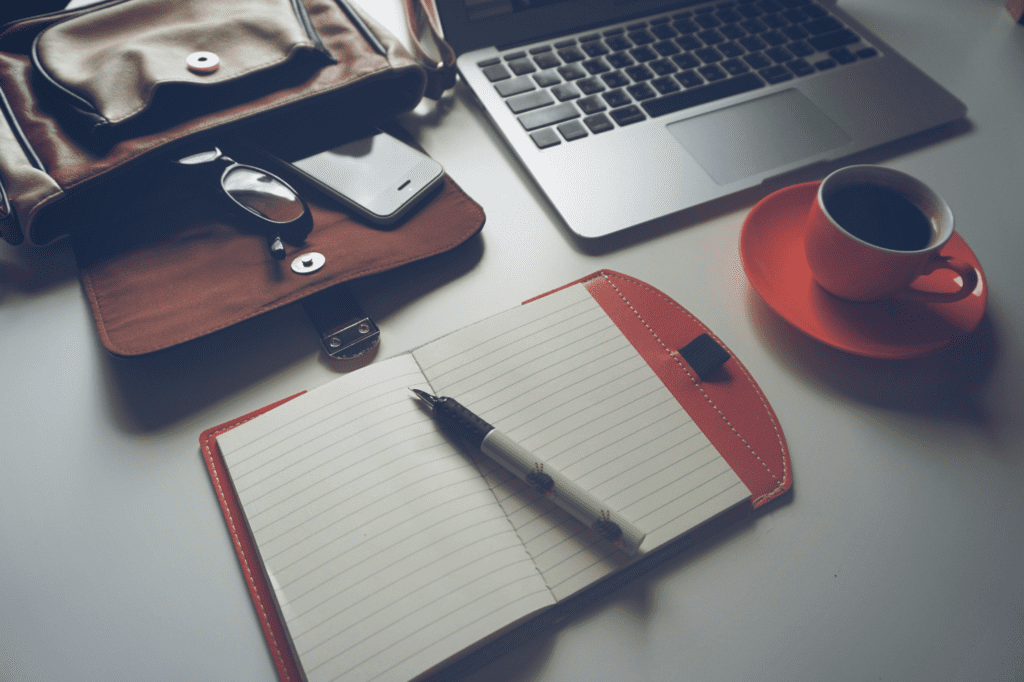 Laptop, glasses, notepad, and cup lying on a table. 